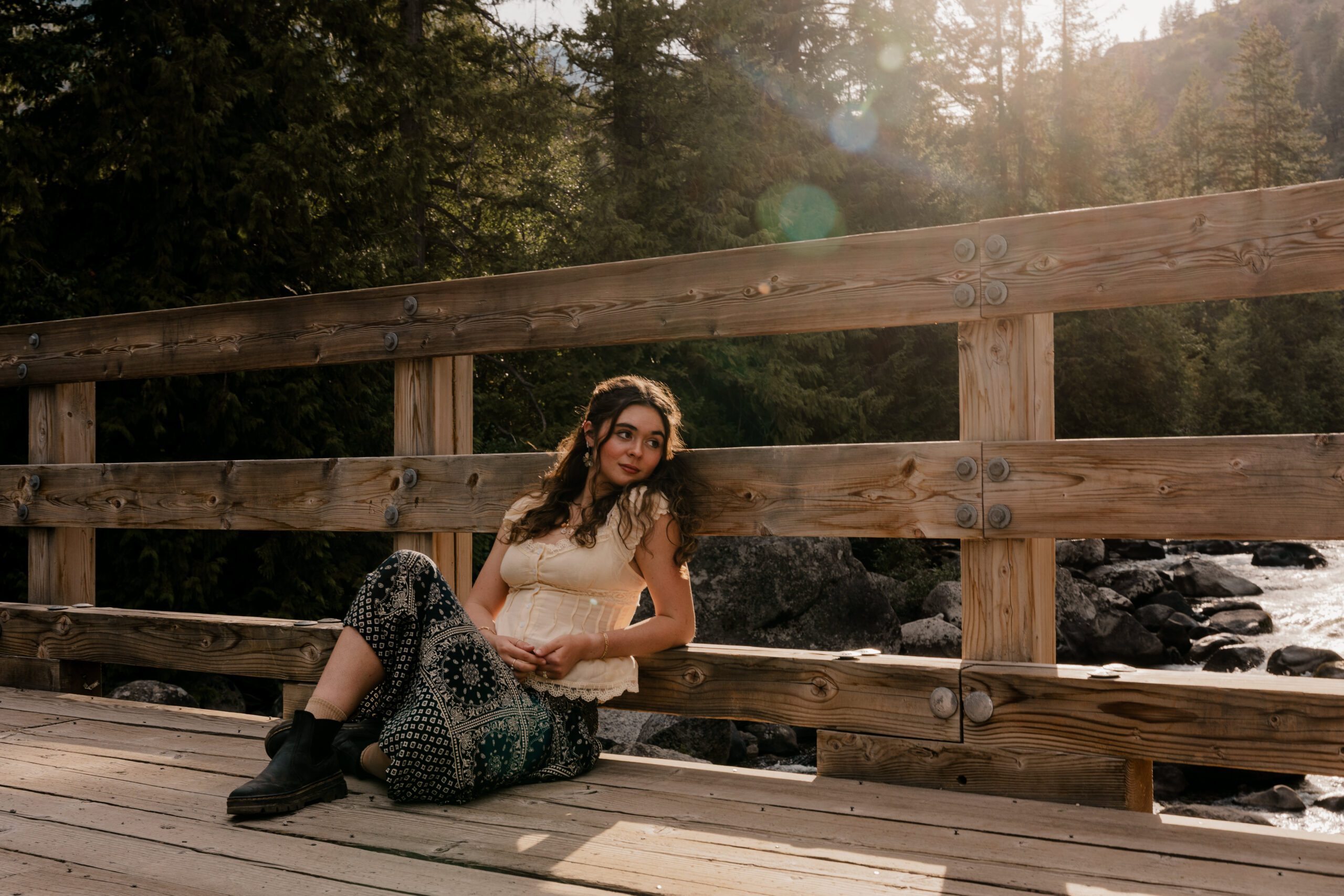 Senior portraits for girl sitting on a wooden bridge in the forest during golden hour in Leavenworth, Washington