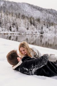 A newly engaged couple rolls around in the snow as they celebrate their engagement
