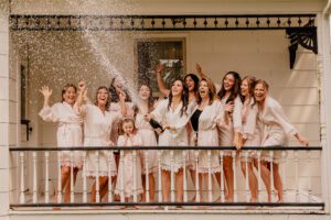 Bride popping a bottle of champagne on the porch of the house at Machias Meadows